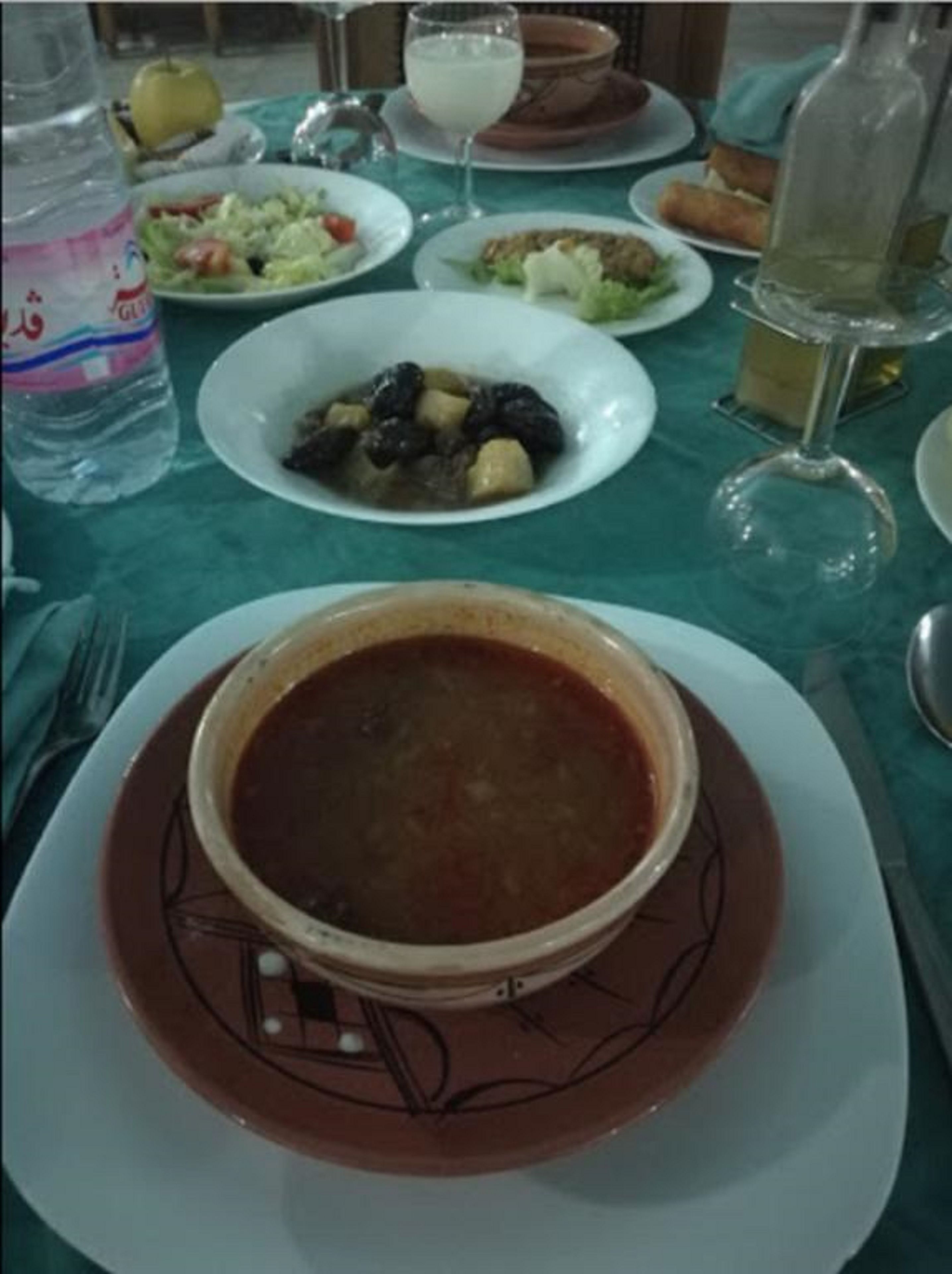 A dining table with various dishes, including a bowl of soup, a plate of olives, and a glass of water.