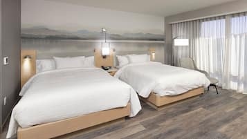 A hotel room with two beds, a view of a lake, and a chair by the window.