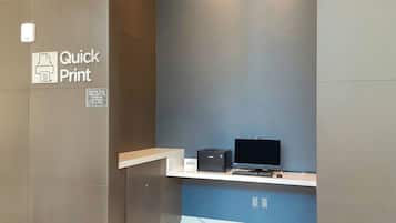 A modern room with a blue accent wall, a white shelf with a printer and a laptop, and a sign indicating a quick print service.