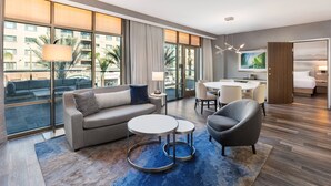 A modern hotel room with a sofa, armchair, and round tables. Large windows offer a view of the cityscape. - Courtyard by Marriott Los Angeles Monterey Park (Monterey Park)