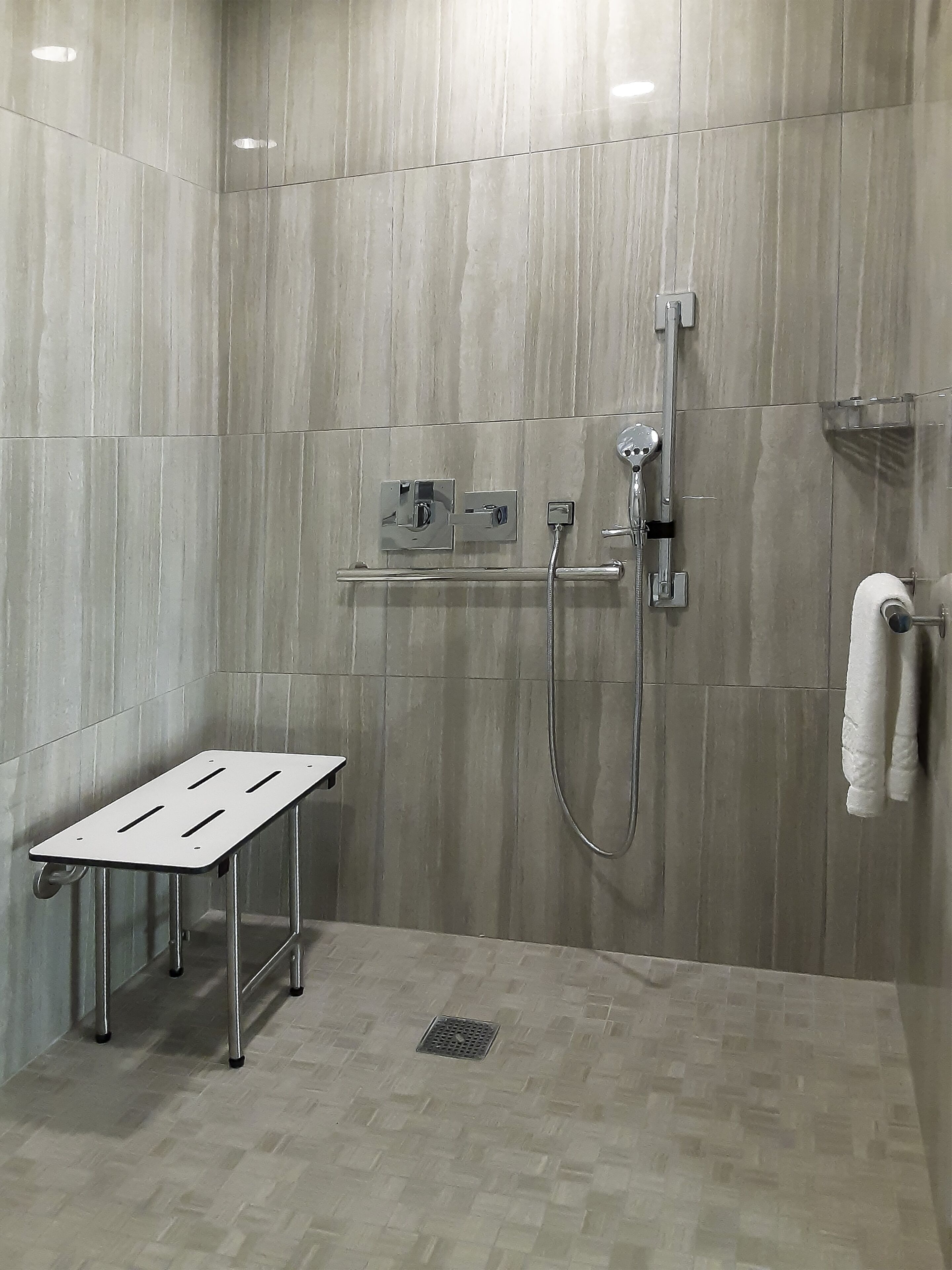 Ein modernes Duschbad mit Handbrause, Handtuchhalter und einem Metallregal.