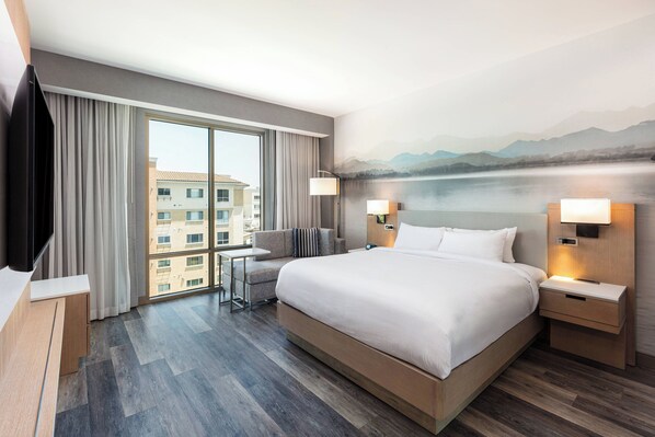 Habitación de hotel con una cama grande, un escritorio y vistas a un edificio a través del ventanal.