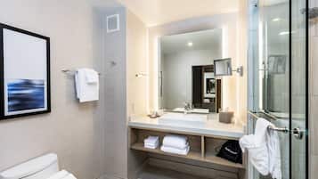 Un baño moderno con un espejo grande, cabina de ducha de vidrio y lavamanos blanco.