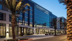 A modern hotel with a glass facade, palm trees, and a well-lit entrance. - Courtyard by Marriott Los Angeles Monterey Park (Monterey Park)