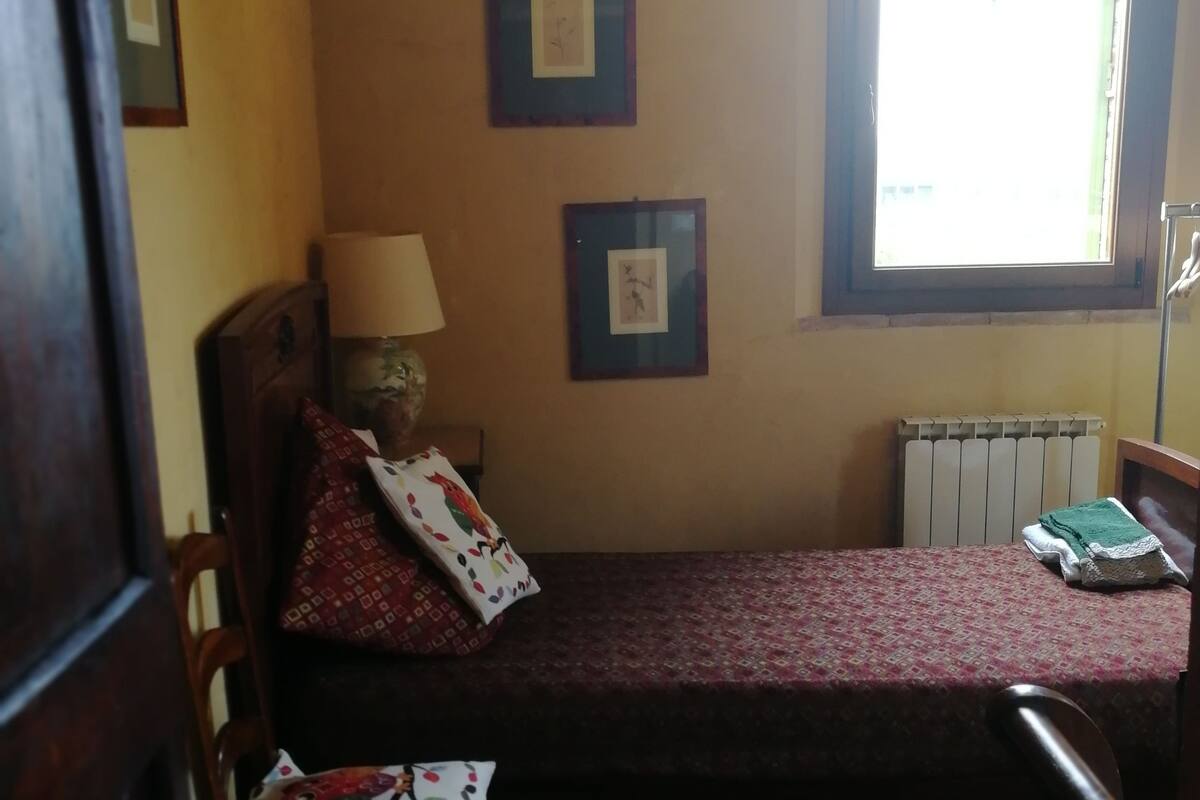 A small, cozy room with a single bed, a chair, a radiator, and two framed pictures on the wall.