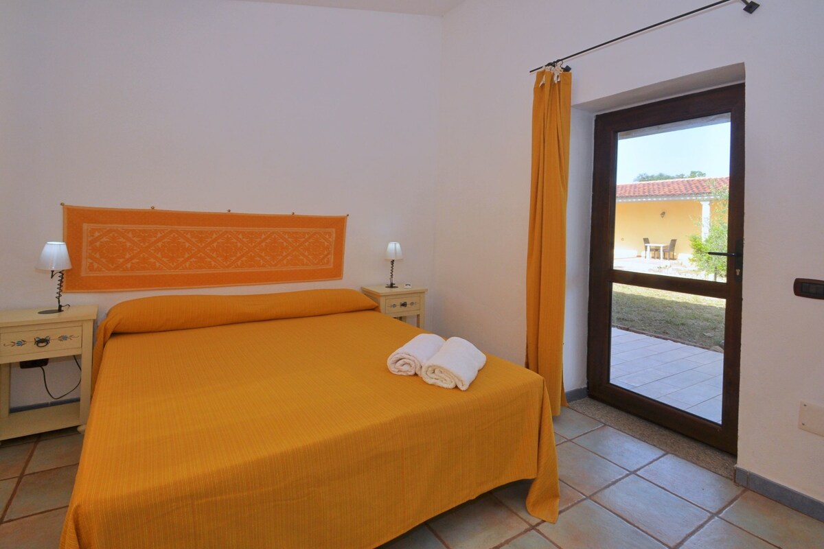 A room with a bed, two bedside tables with lamps, a window with curtains, and a view of the outside.