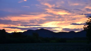 Un coucher de soleil sur un paysage montagneux, avec un champ au premier plan.
