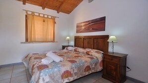 Une chambre à coucher avec un lit en bois, deux tables de chevet avec des lampes, une fenêtre avec des rideaux et un tableau accroché au mur.