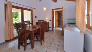 Un coin repas avec une table et des chaises en bois, une petite cuisine équipée d’un réfrigérateur et une fenêtre avec des rideaux.