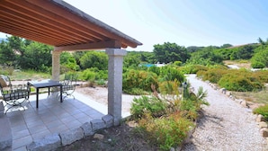 Une terrasse extérieure dotée d’une pergola, de piliers en pierre et d’une table avec des chaises.
