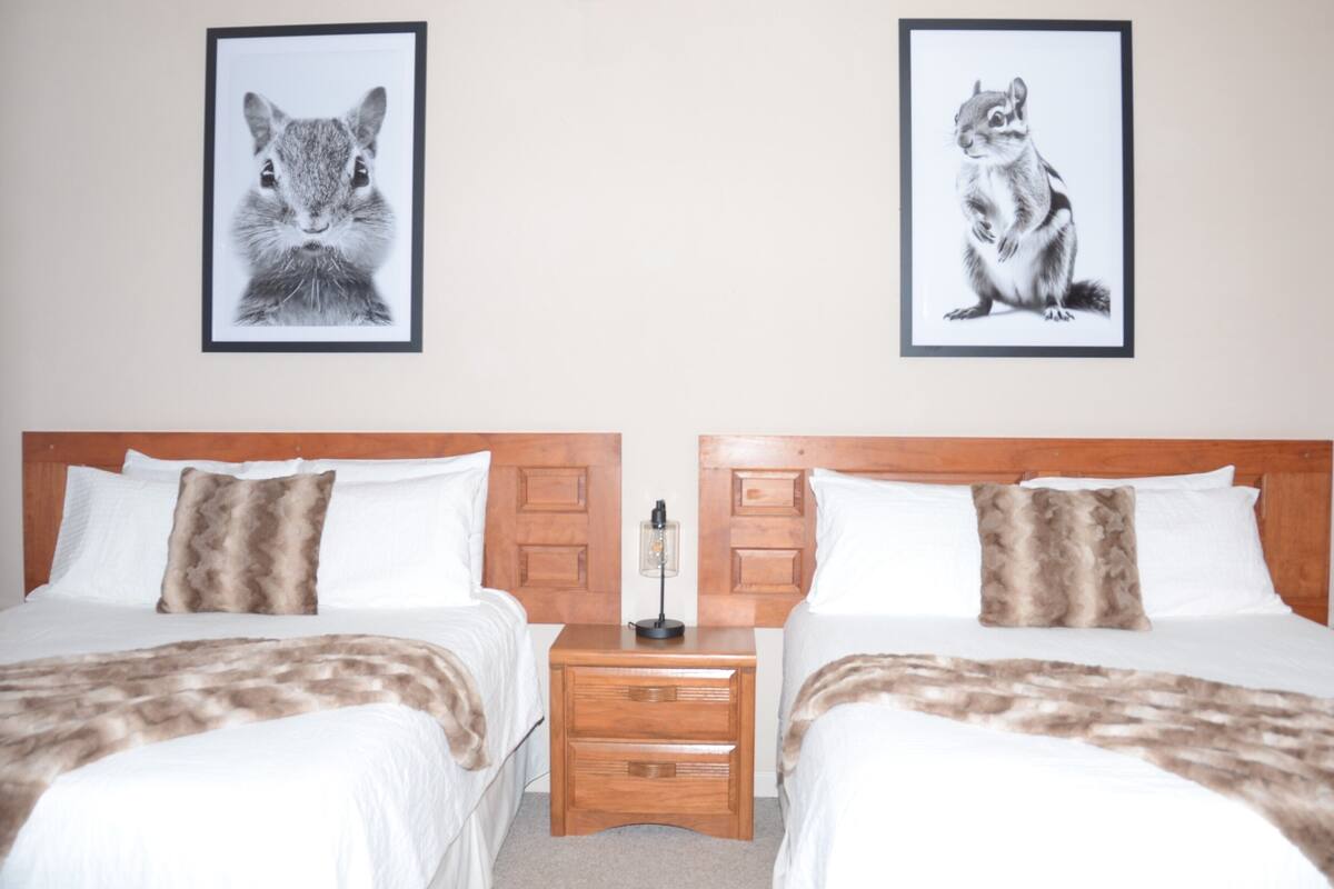 Een hotelkamer met twee bedden, een nachtkastje en twee ingelijste foto’s van dieren aan de muur.