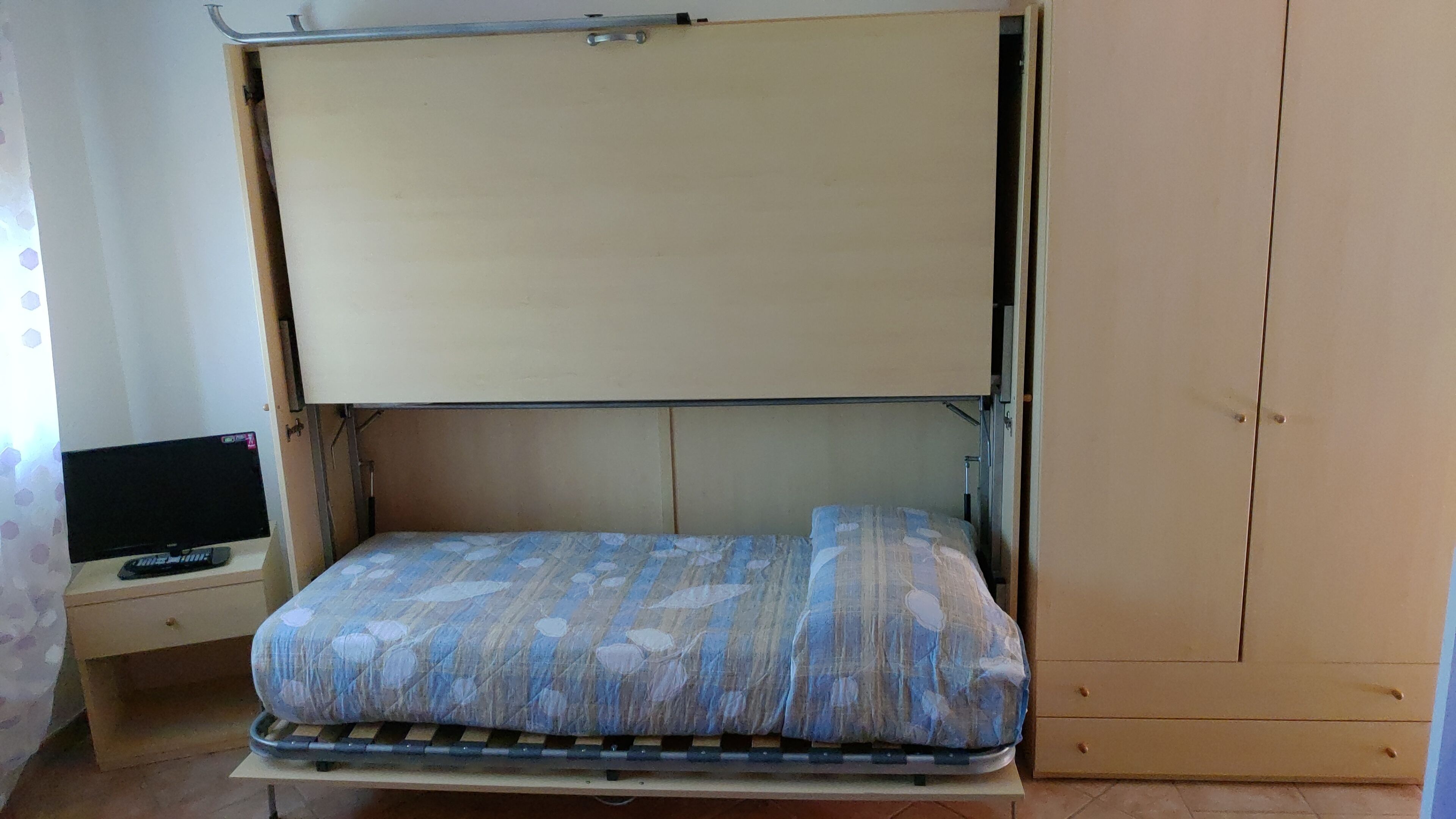 Una habitación pequeña con cama, una mesita y televisor, y un armario.