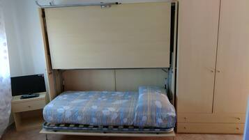 Una habitación pequeña con cama, una mesita y televisor, y un armario.