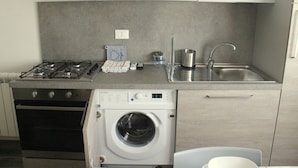 Une cuisine compacte équipée d’une cuisinière à gaz, d’un four, d’un lave-linge, d’un évier et de placards.