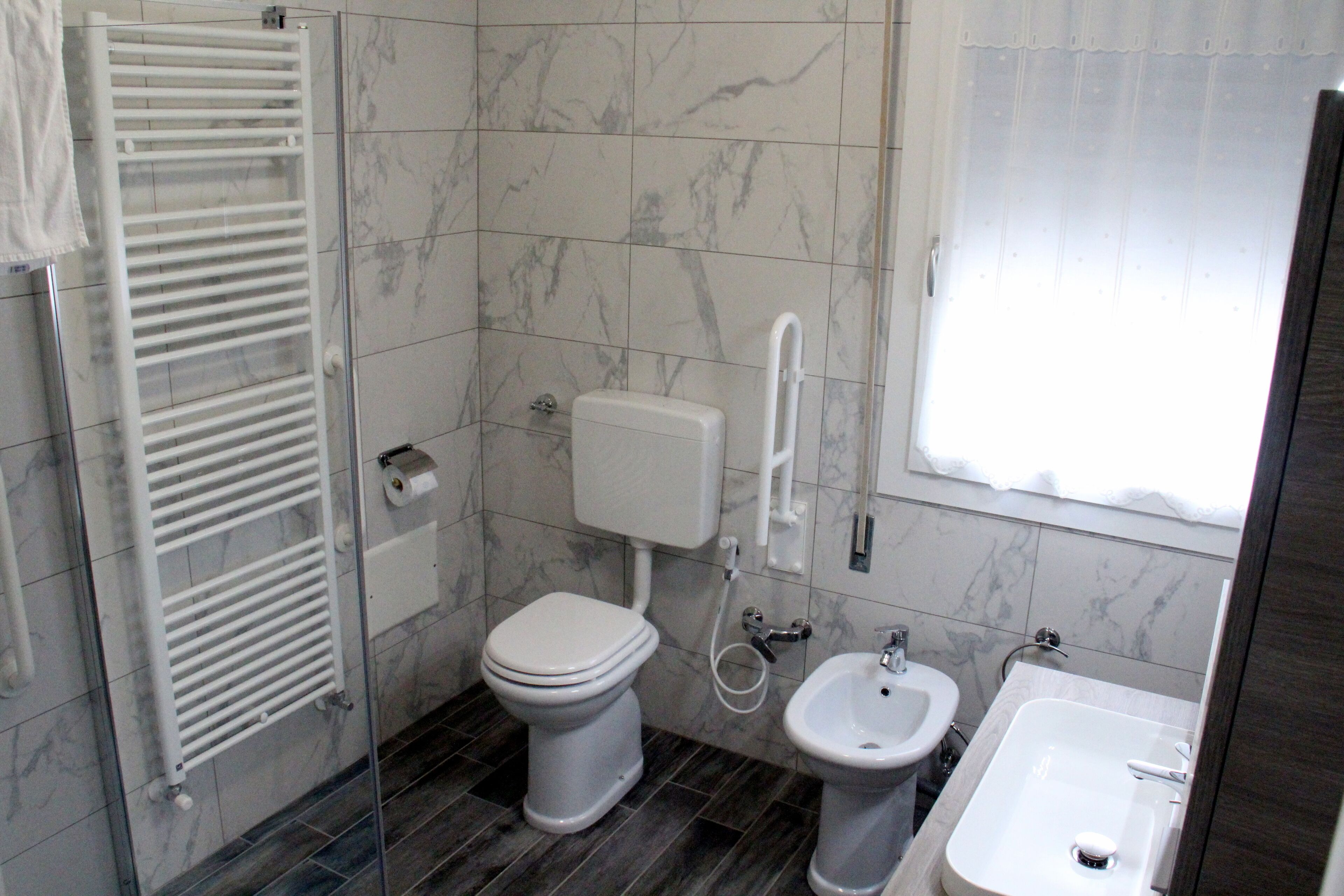 Un baño con inodoro, bidé y lavamanos, baldosas de mármol y cabina de ducha de cristal.