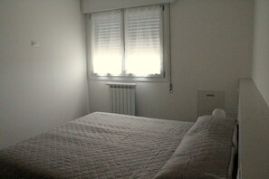 A small, simple bedroom with a single bed, a window with blinds, and a radiator. - Agriturismo La Fraterna (Porto Tolle)
