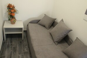 A grey sofa with multiple cushions, a small white side table, and a decorative vase with flowers. - Agriturismo La Fraterna (Porto Tolle)