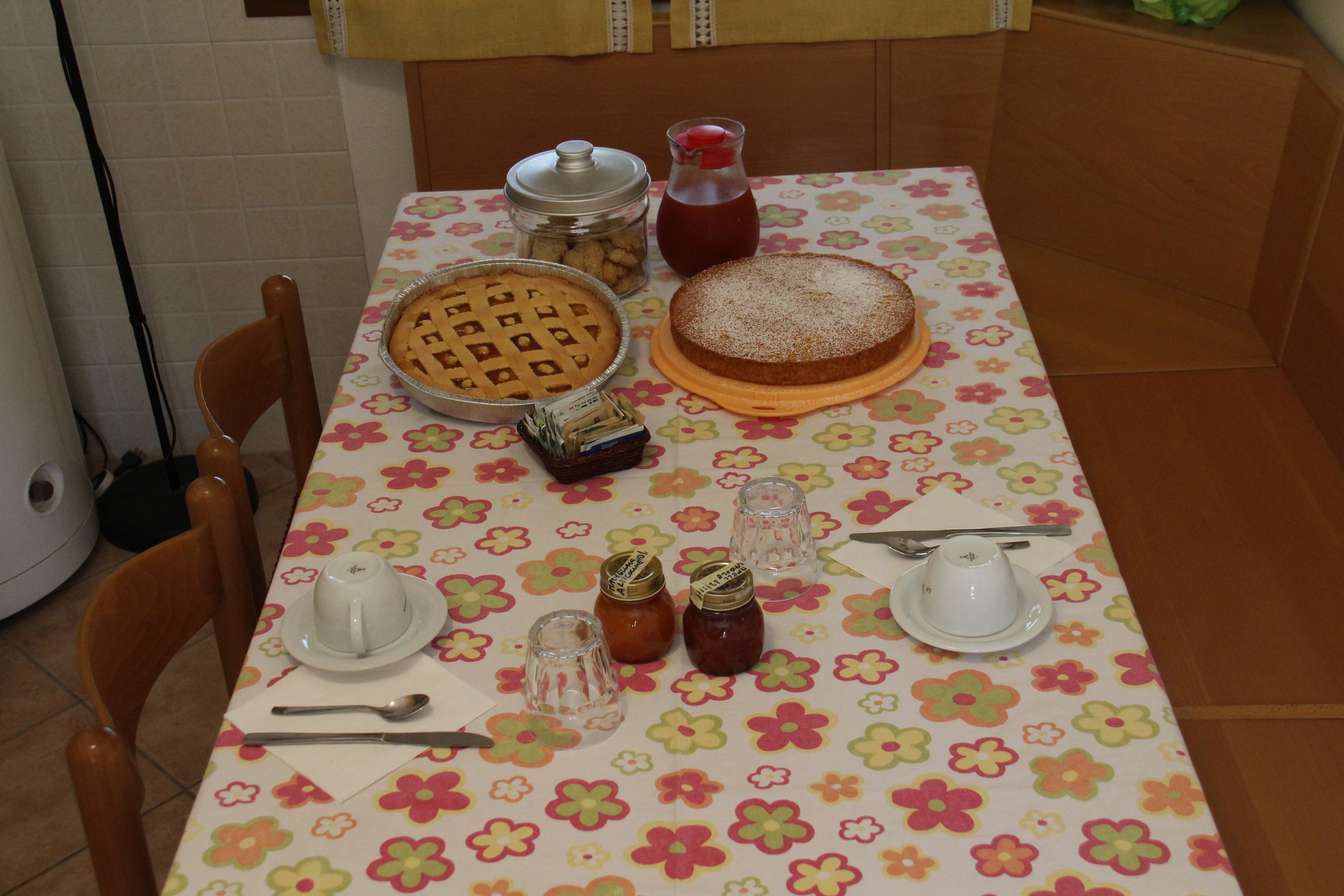 A table set with a floral tablecloth, a pie, a jar of jam, and a pitcher of juice.