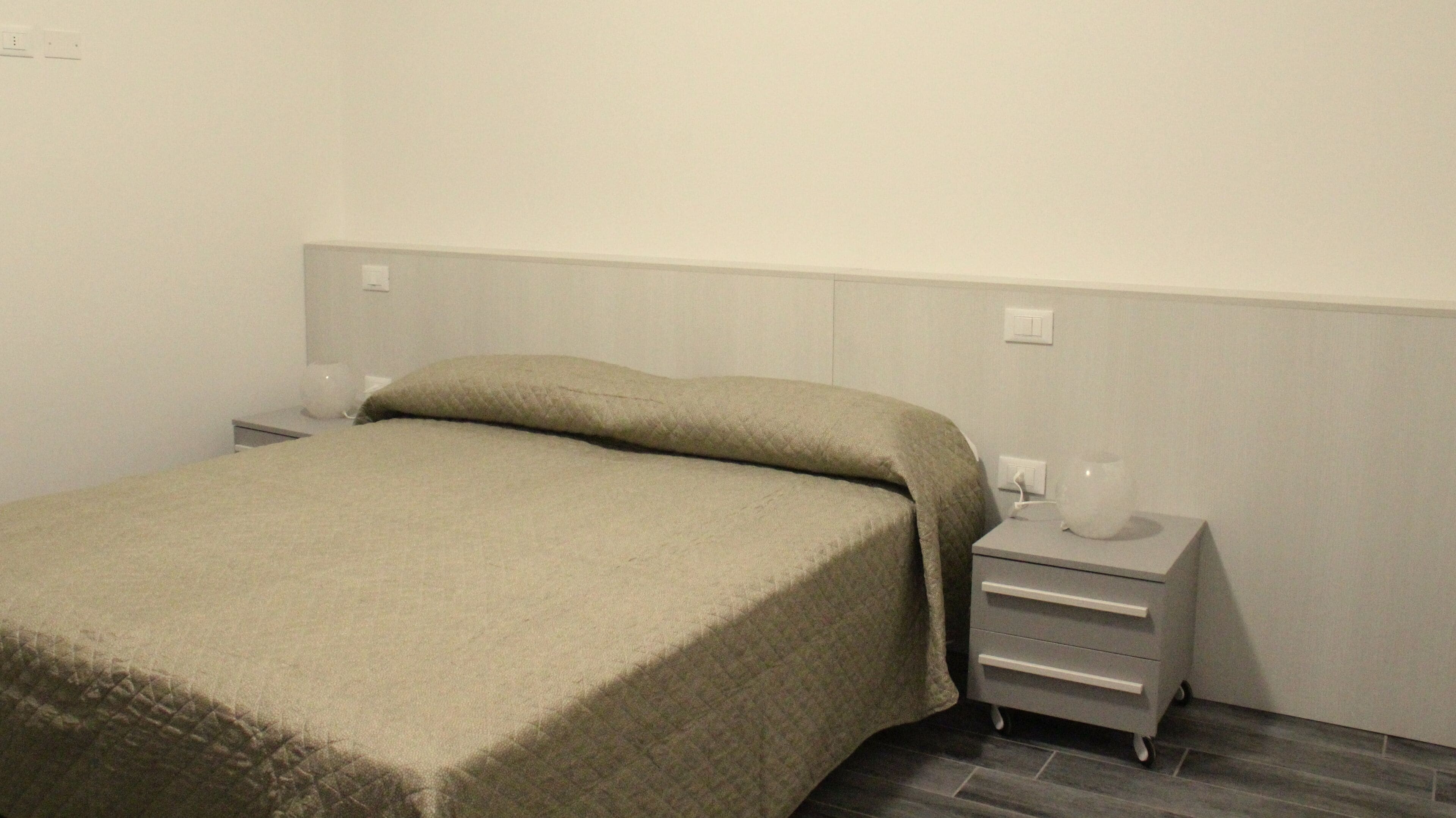 Yksinkertainen ja siisti hotellihuone, jossa on sänky, yöpöytä ja pieni sivupöytä.