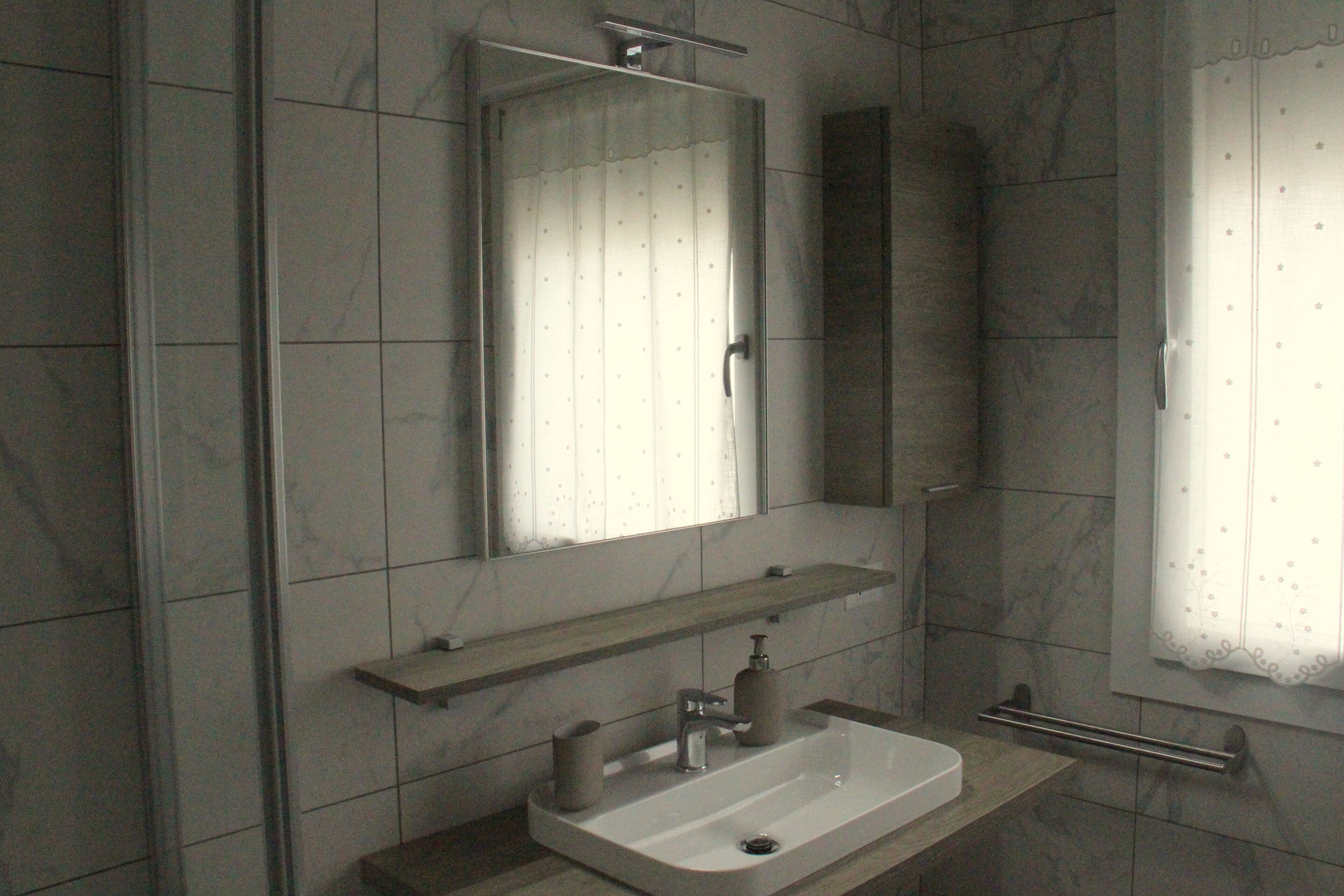 A bathroom with a large mirror, a sink, and a towel rack.