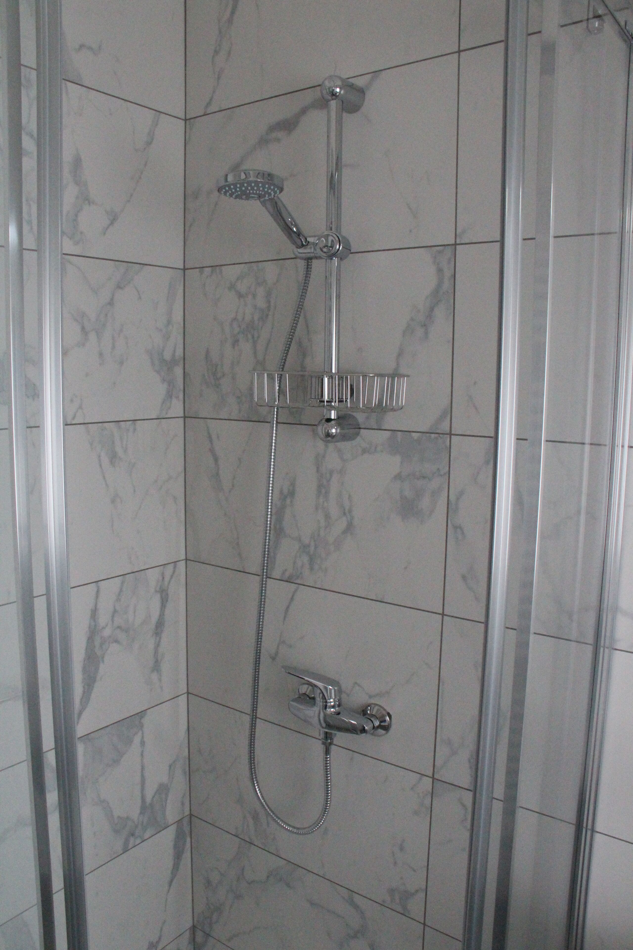 Ducha con cabezal de ducha manual y grifo empotrado en un cuarto con paredes de azulejos de mármol.