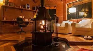 A cozy living room with a wood-burning stove, a comfortable sofa, and a brick wall. - Pousada Ricanto Amore Mio (Camanducaia)