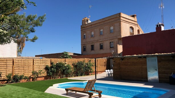 A swimming pool with a wooden deck and lounge chair, surrounded by a well-maintained lawn and a brick wall. - VUT Rural Dulcinea de la Mancha Pool Wifi (Fernán Caballero)