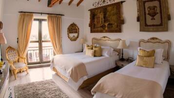 A hotel room with two beds, a large window with curtains, a chair, and wall-mounted artwork.