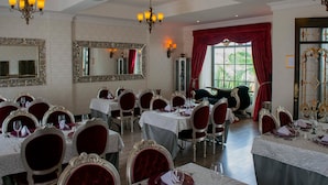 Een formele eetzaal met meerdere tafels en stoelen, kroonluchters en grote spiegels.