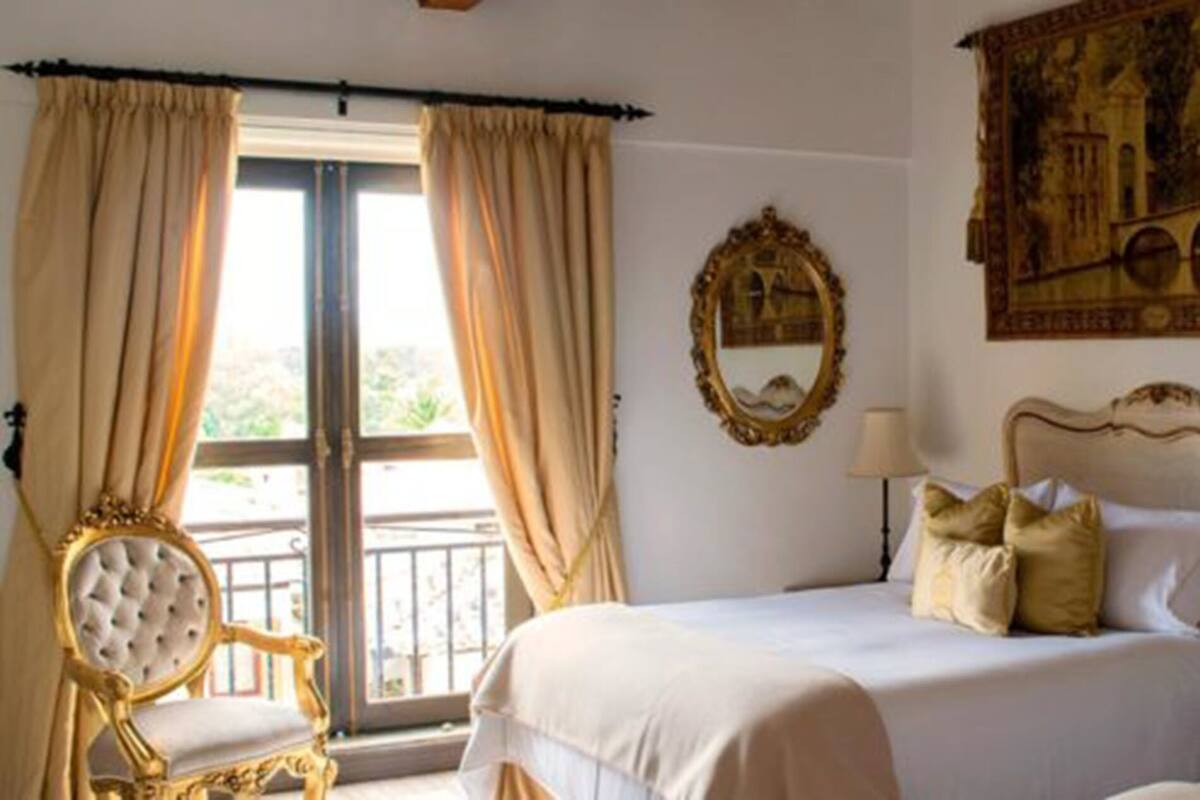 Ein Hotelzimmer mit zwei Betten, einem großen Fenster mit Vorhängen, einem dekorativen Spiegel und einem Bild an der Wand.