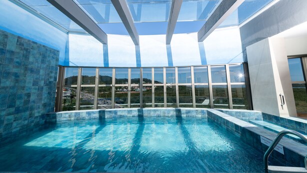 Una piscina interior moderna con techos de vidrio transparente y vistas del paisaje circundante.