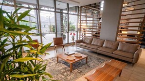 Una sala moderna con sofá, mesa de centro y sillones. Se aprecia un ventanal con vistas al exterior.
