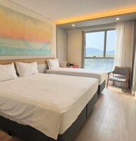 Ett hotellrum med två sängar, ett stort fönster med utsikt och en tavla på väggen.