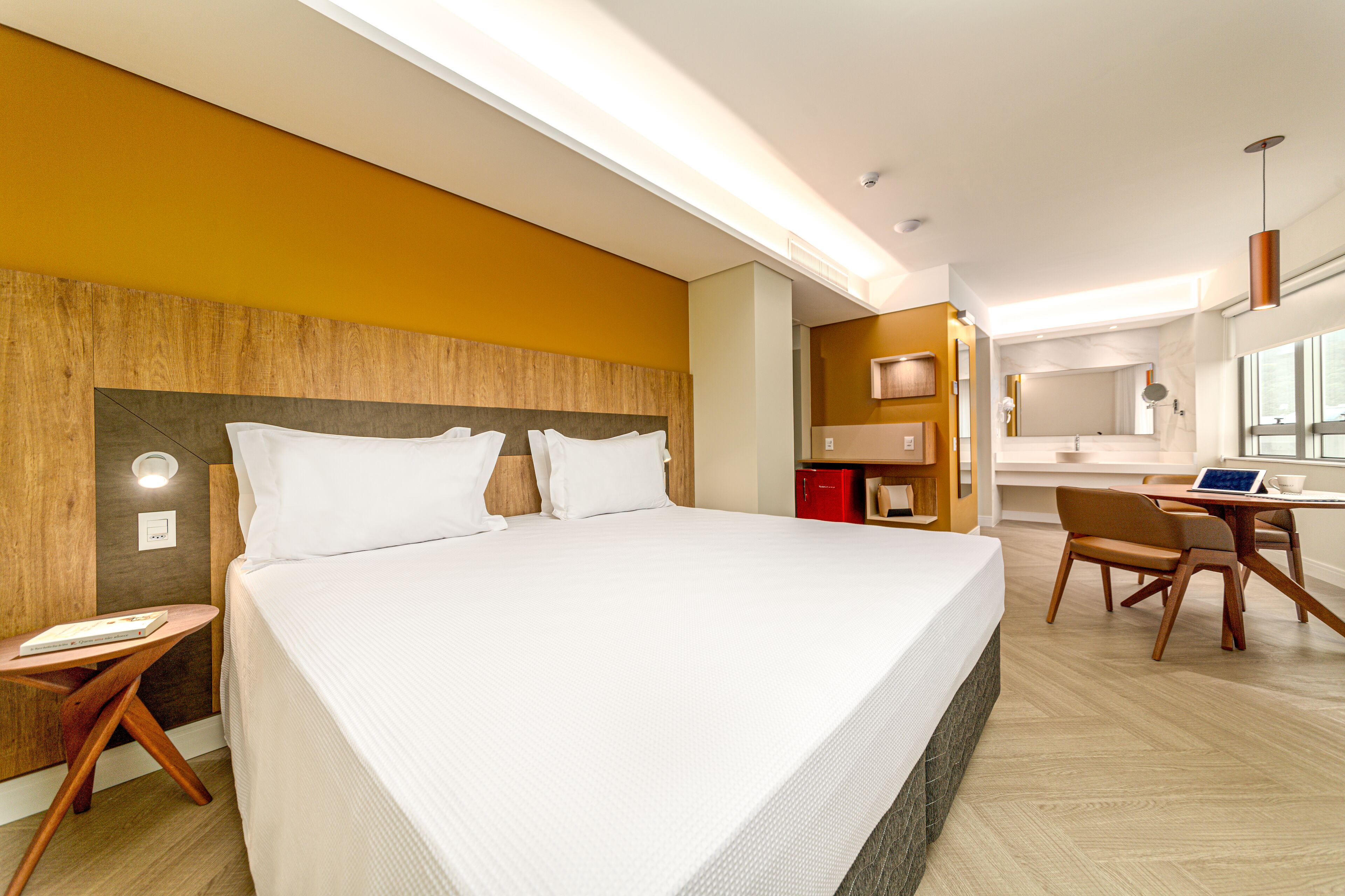 A modern hotel room with a large bed, a desk, and a bathroom visible through an open door.