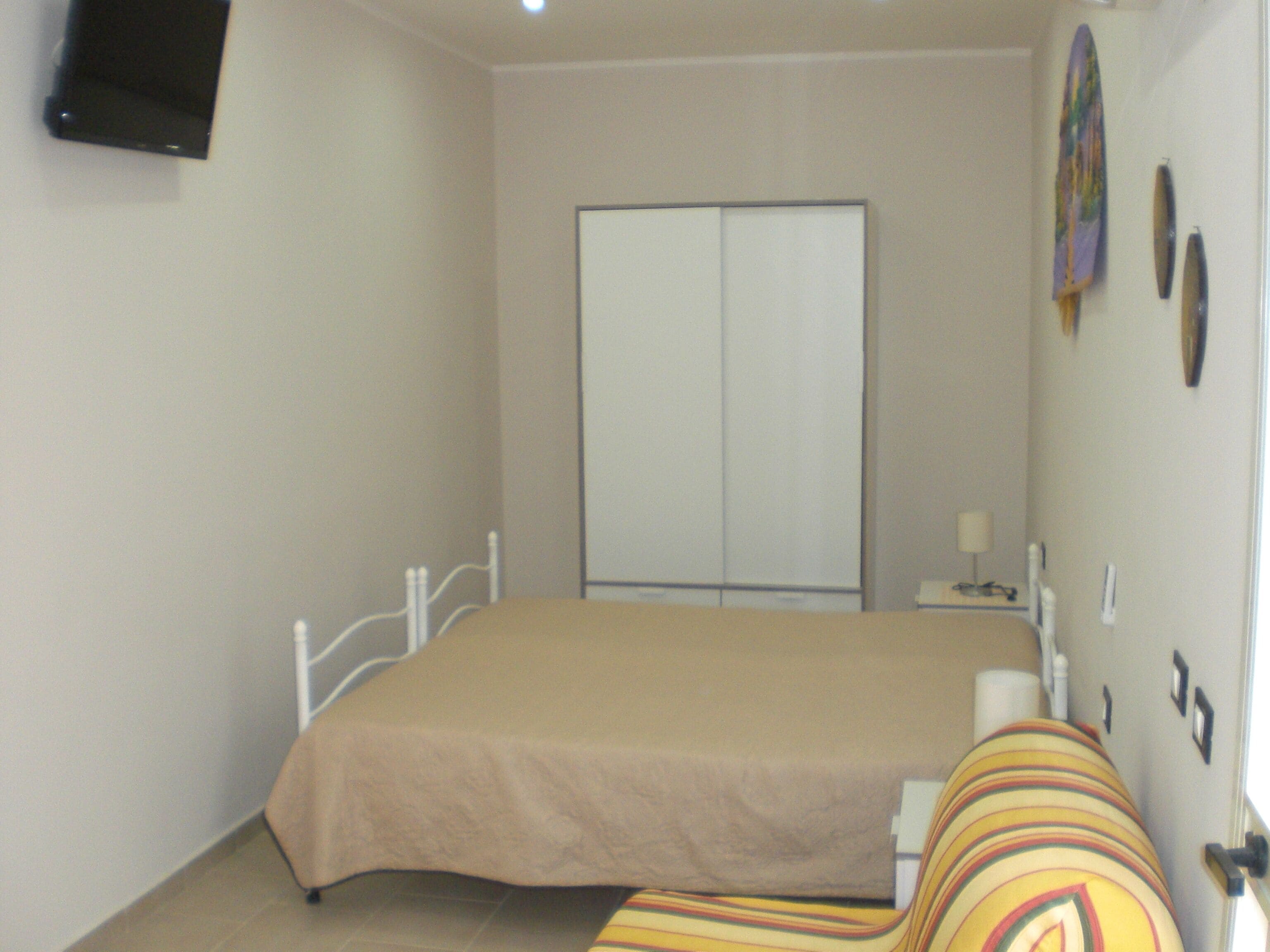 Un dormitorio con cama, armario, mesita de noche y televisor montado en la pared.