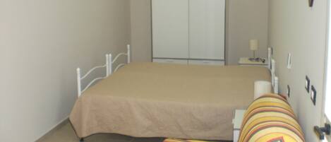 Un dormitorio con cama, armario, mesita de noche y televisor montado en la pared.