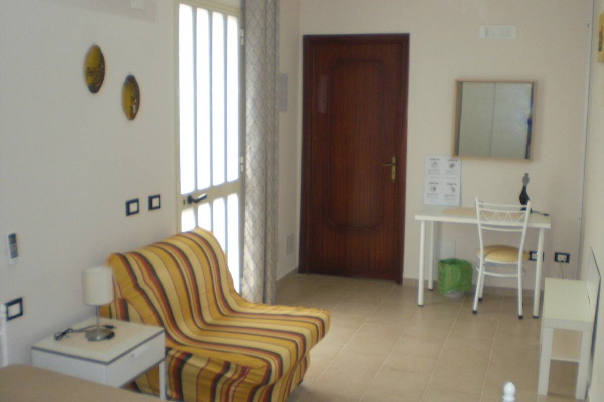 Une pièce avec un canapé à rayures, une petite table, un bureau avec une chaise et une porte.