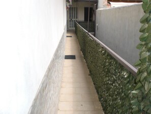 A narrow, paved corridor with a tiled floor, bordered by a low stone wall on one side and a white wall on the other. - Giò & Giò (Riposto)