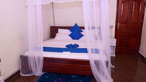 A neatly made bed with a canopy, a bedside table, and a pair of slippers on a blue mat. - Zebra Tourism  Hotel (Kigali)