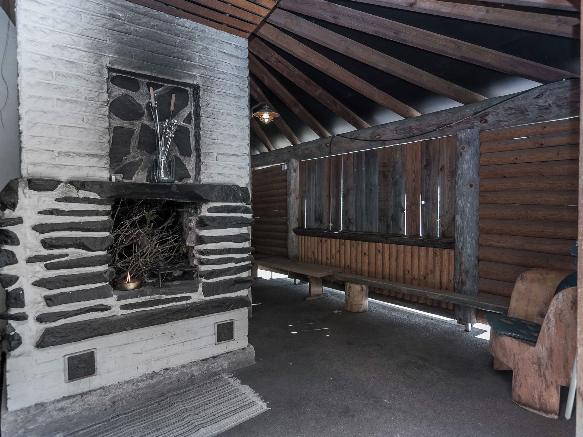 A rustic cabin interior with a stone fireplace, wooden benches, and a sloped ceiling.