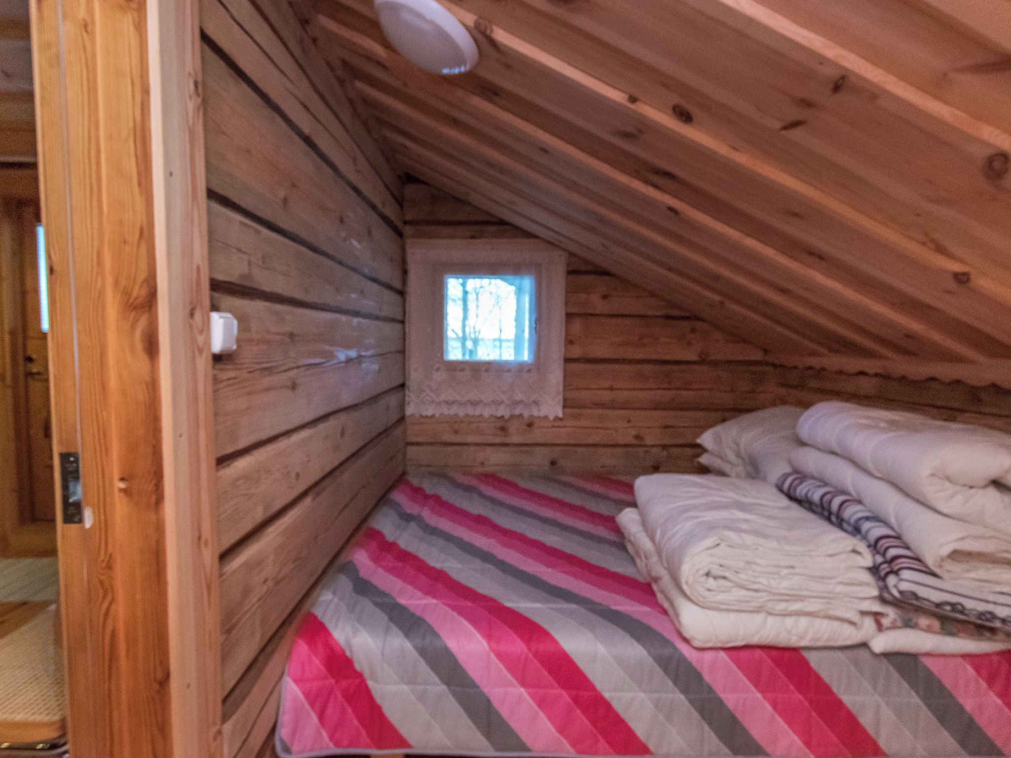 Ein kleines, gemütliches Schlafzimmer im Dachgeschoss mit Holzwänden, einem Fenster und einem Bett mit gestreifter Bettwäsche.