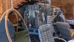 Ein gemütliches Blockhaus-Interieur mit Kamin aus Stein, Holzwänden, einer Holztreppe und einem Hängesessel.