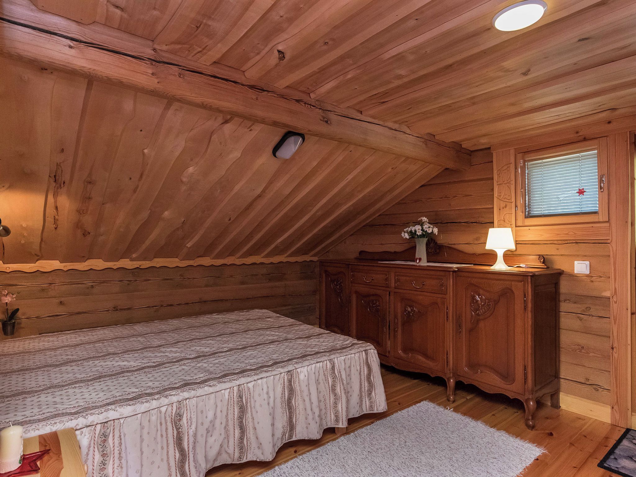 Quarto de madeira com cama, cômoda e janela com persianas.