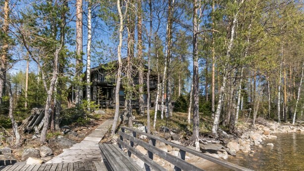 Eine Holterrasse führt zu einer Hütte, umgeben von Bäumen und einem Fluss.