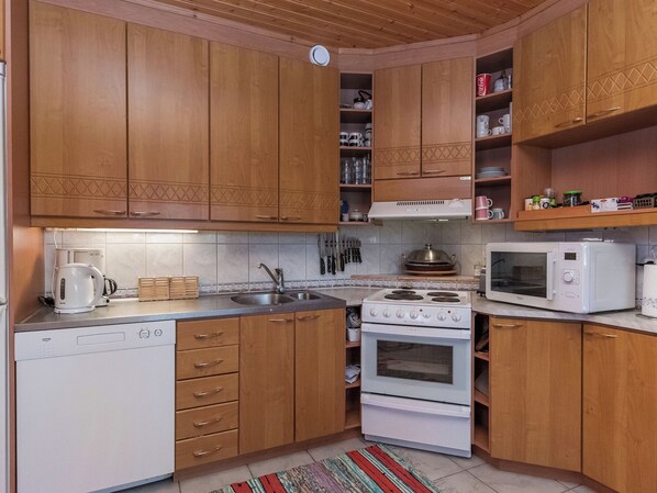 Una cocina con armarios de madera, lavavajillas blanco, estufa, microondas y fregadero.
