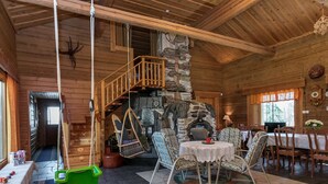 Ein gemütliches Blockhaus-Interieur mit Kamin aus Stein, einem Holzespeisesaal und einem Hängekorbstuhl.