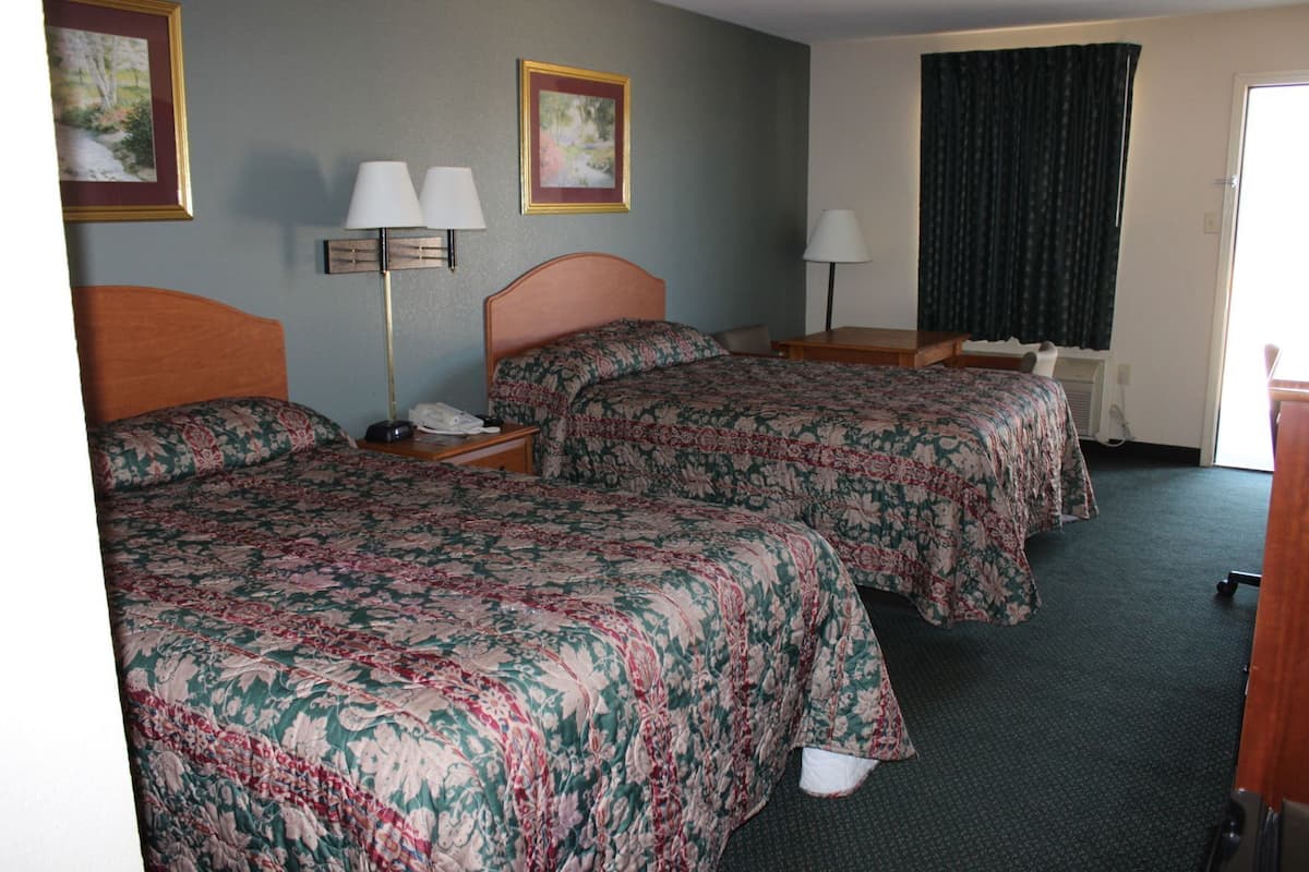 A hotel room with two beds, a desk, a chair, a lamp, and a window with curtains.