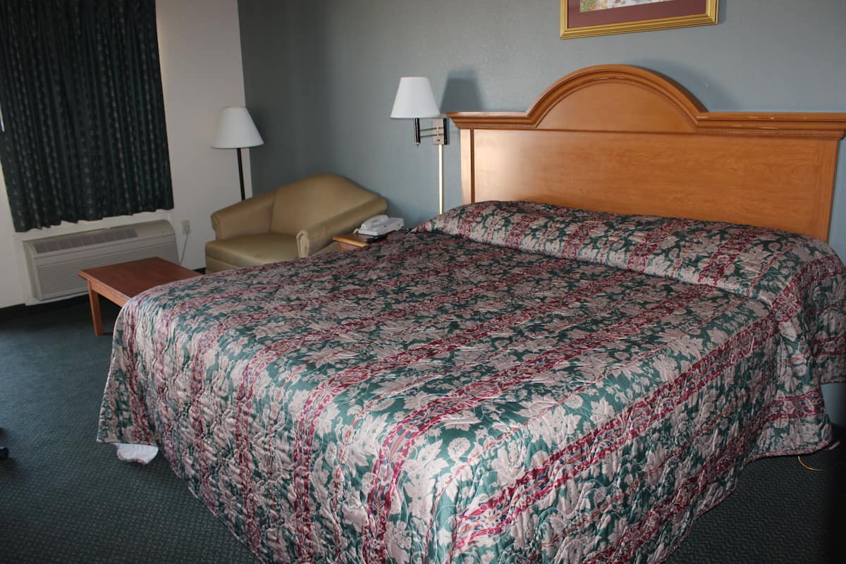 A hotel room with a bed, a chair, a lamp, and a wall-mounted phone.