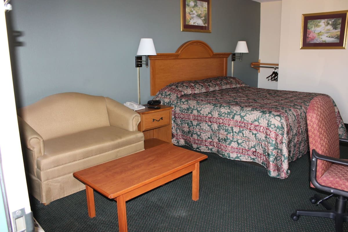 A hotel room with a bed, a chair, a small table, a nightstand, and two wall-mounted lamps.