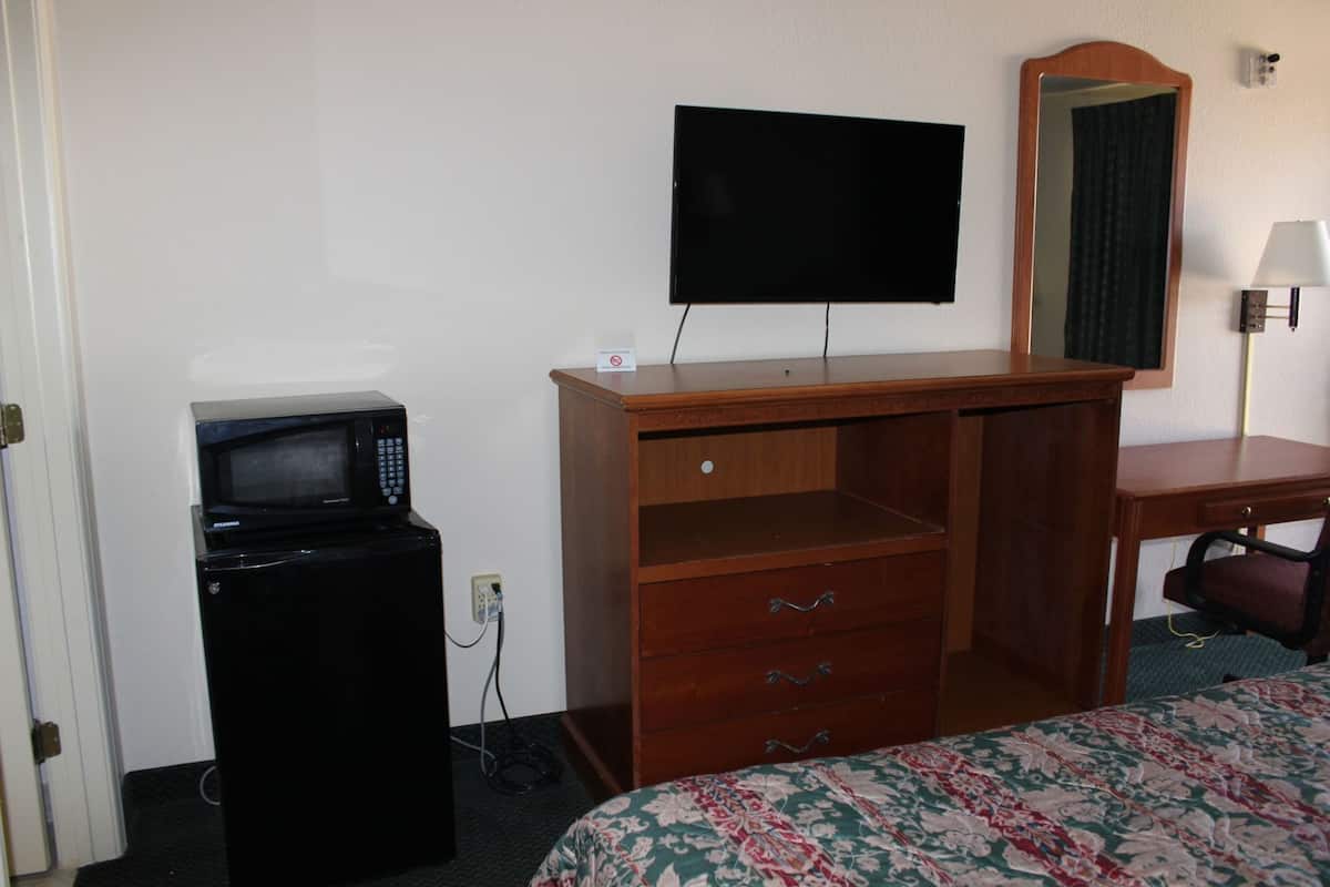 A hotel room with a bed, a desk with a mirror, a television, a microwave, and a lamp.
